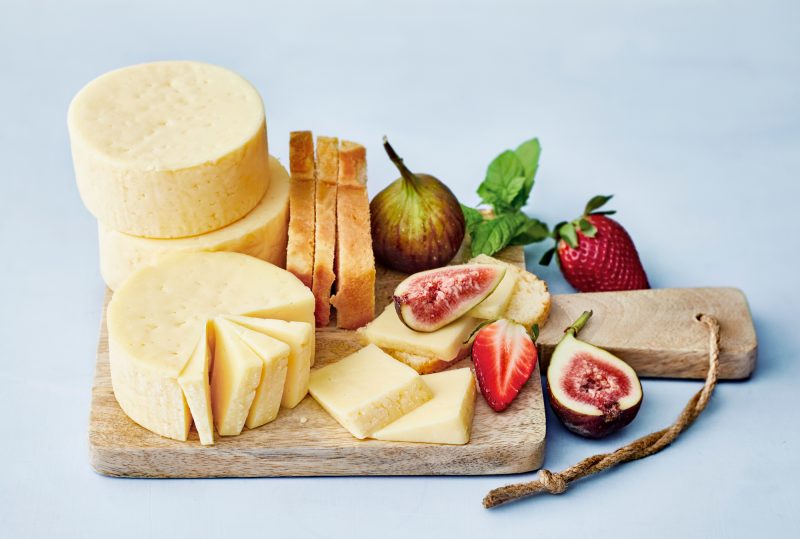 Kuvassa puisella leikkuulaudalla on Oltermanni juustokiekkoja, tuoretta viikunaa ja mansikkaa sekä leivän siivuja.