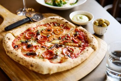 Ravintola Bloccon paistama kokonainen pyöreä salsicciapizza pöydällä, sivuilla oliiveja ja tahnaa.